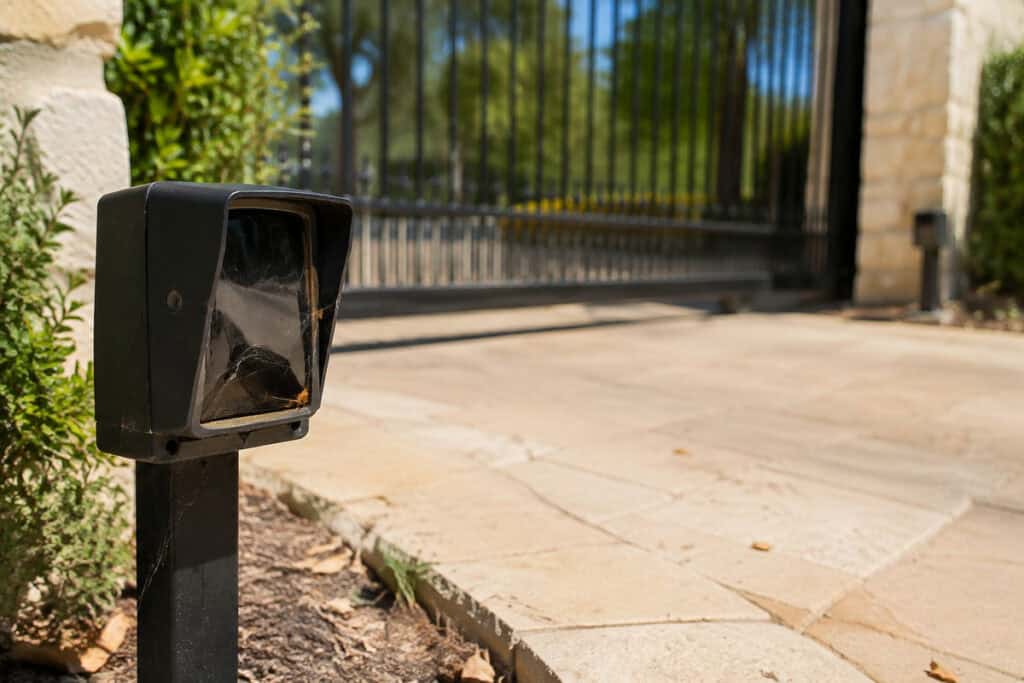 Spider web partially blocking a photo-eye safety sensor beside a residential sliding gate